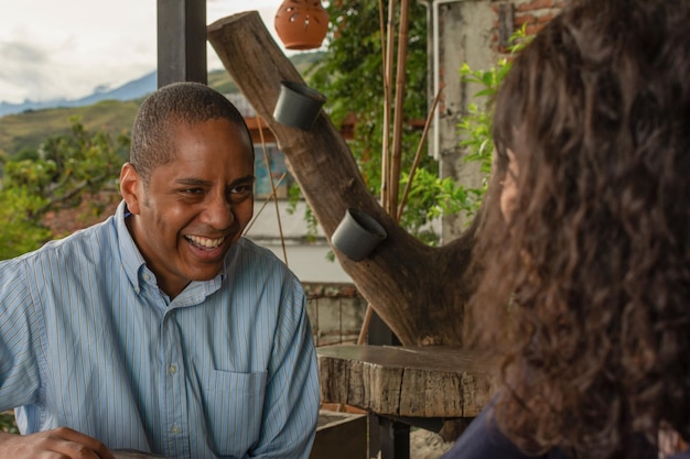 A close-up photo of a Brazilian IBGE census worker interviewing a resident in a rural area of Brazil. The enumerator is holding a tablet and the resident is smiling and engaged, showing the interaction between them during the census. The environment is a simple, rural house.