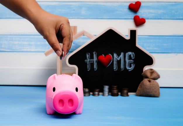 A hand placing a coin into a piggy bank with a house-shaped opening on top. In the background, there are charts and graphs illustrating investment growth and diversification, with the year 2025 highlighted.