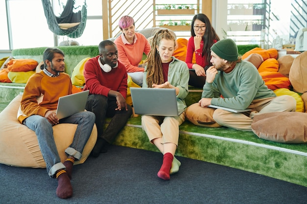 A diverse group of students collaborating on a project in a modern, high-tech classroom setting. They are using tablets and laptops, and the atmosphere is energetic and collaborative.