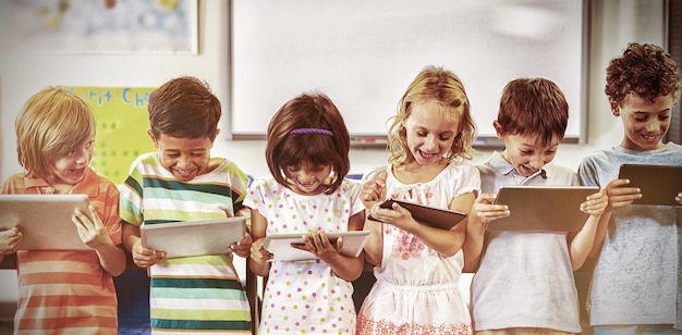 A cheerful group of elementary school students using tablets in a brightly lit classroom, with the teacher guiding them, showcasing the application of educational apps in early childhood education and promoting collaborative learning.