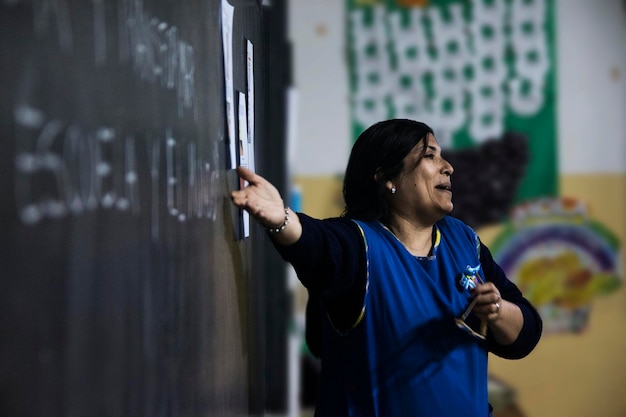 A Brazilian teacher in a poorly lit and overcrowded classroom, pointing to a chalkboard. The image should convey the challenging conditions faced by many educators in Brazil's public schools.
