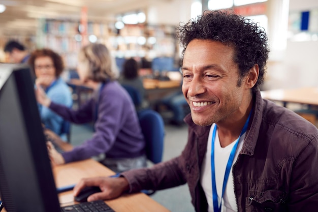 An adult student smiling while working on a laptop in a computer lab, surrounded by other students engaged in learning activities. The setting is a modern educational environment, emphasizing the access to technology provided by EJA.