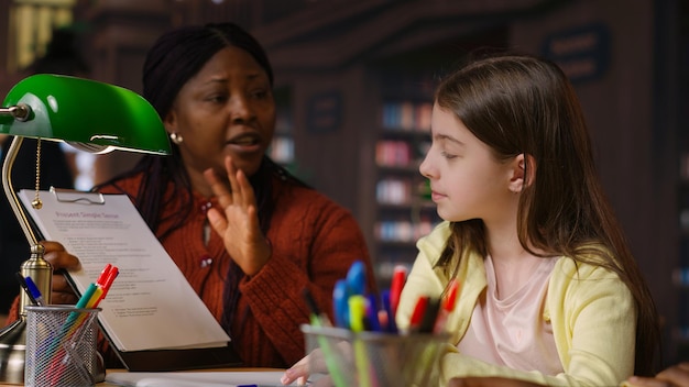 A female teacher helping an adult student with their work in a small classroom setting. The teacher is giving personalized attention, demonstrating the supportive environment of EJA.