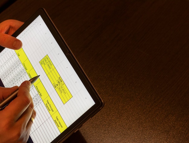 A close-up of hands working on a detailed financial spreadsheet, highlighting the columns of numbers and calculations. The image focuses on the intersection of technology and finance.
