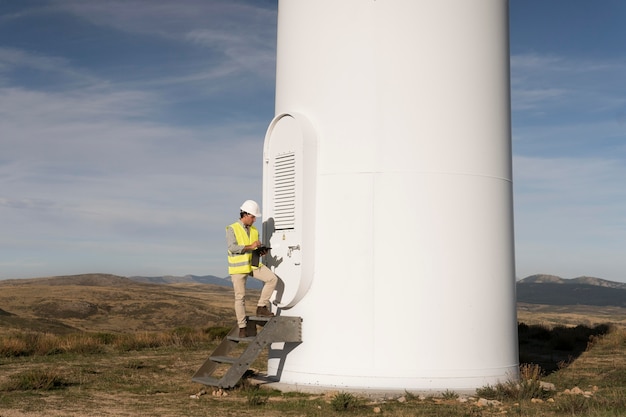 A close-up shot of a technician in a hard hat inspecting a large wind turbine on a wind farm in northeastern Brazil around sunset.