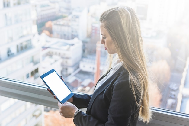 A financial analyst examining graphs on a tablet in a modern office with a window overlooking a city skyline with solar panels integrated within the buildings.
