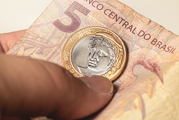 A close-up image of Brazilian currency (Real) being exchanged between a businessperson and a worker, symbolizing the flow of wages and the economic impact of labor laws.