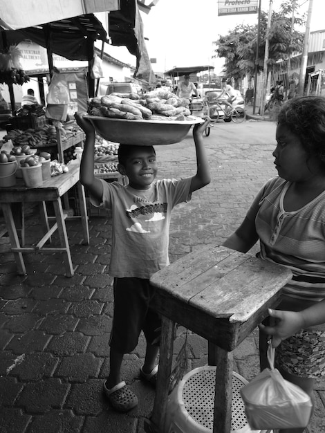 A black-and-white photograph of a bustling Brazilian marketplace, with vendors selling various goods. Capture the lively atmosphere and the diverse interactions between people. Focus on details like handwritten signs with prices and the expressions on people's faces.