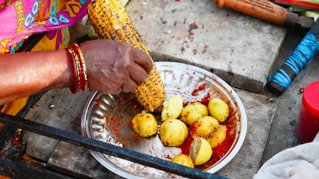 A close-up shot of a woman preparing acarajé in a traditional Bahian street food stall, wearing a colorful traditional dress and beaded necklaces. The acarajé is being fried in a large pan of dendê oil, surrounded by various toppings and ingredients.