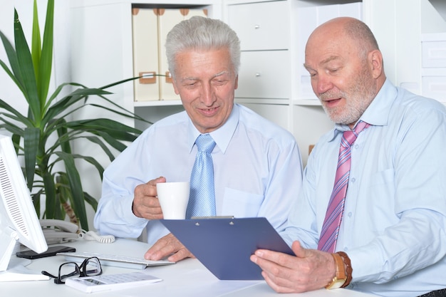 A financial advisor sitting at a desk, discussing retirement plans with a senior client and pointing to charts showing potential investment growth scenarios