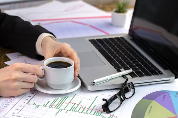 A person working on a laptop with charts and graphs about financial planning displayed on the screen, with a cup of coffee and a notebook nearby.