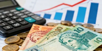 Notas de real e moedas com calculadora e gráfico de juros, representando o crédito no Brasil.